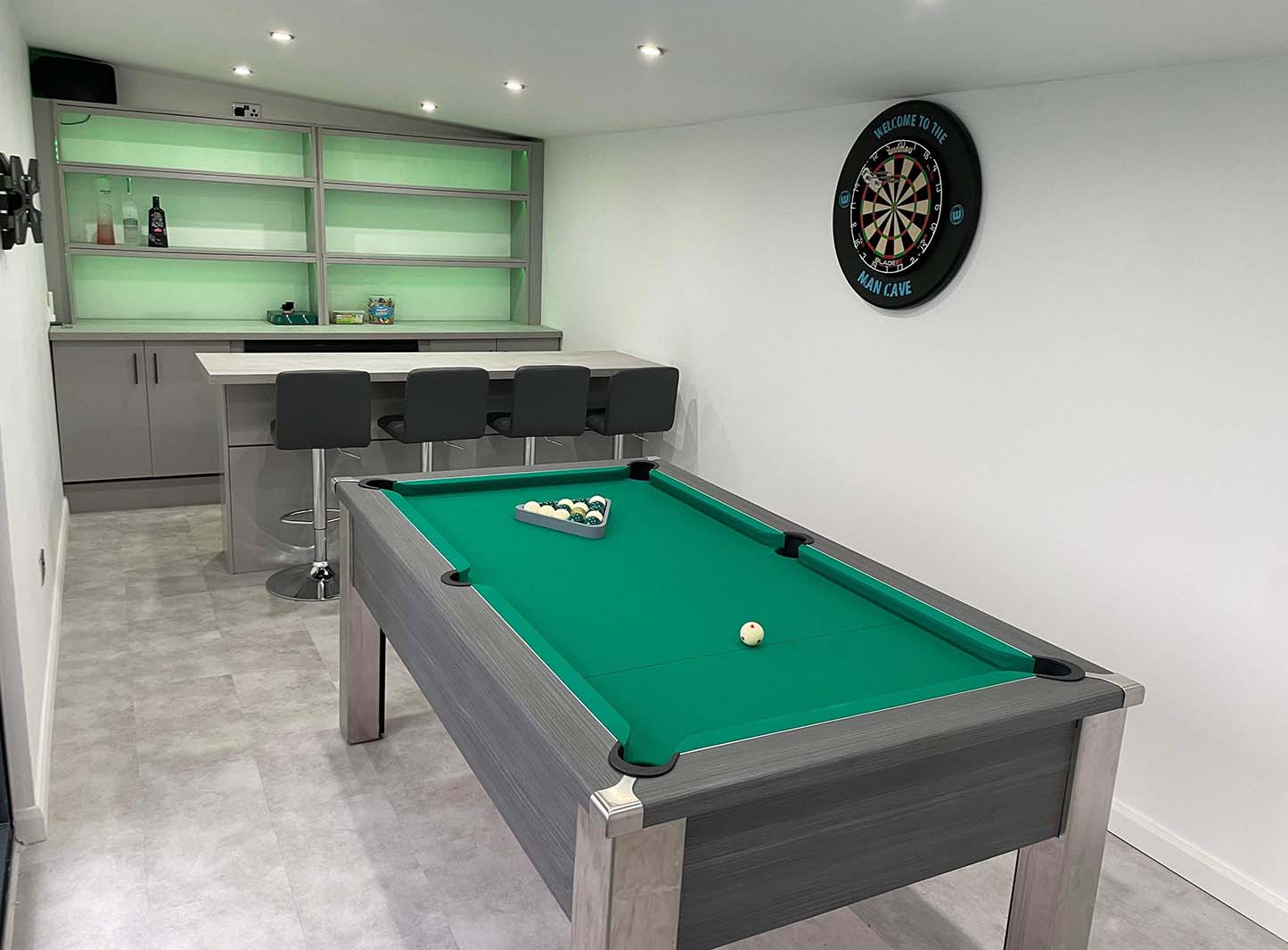 games room in a green theme with a pool table and darts board and bar with dark grey stools