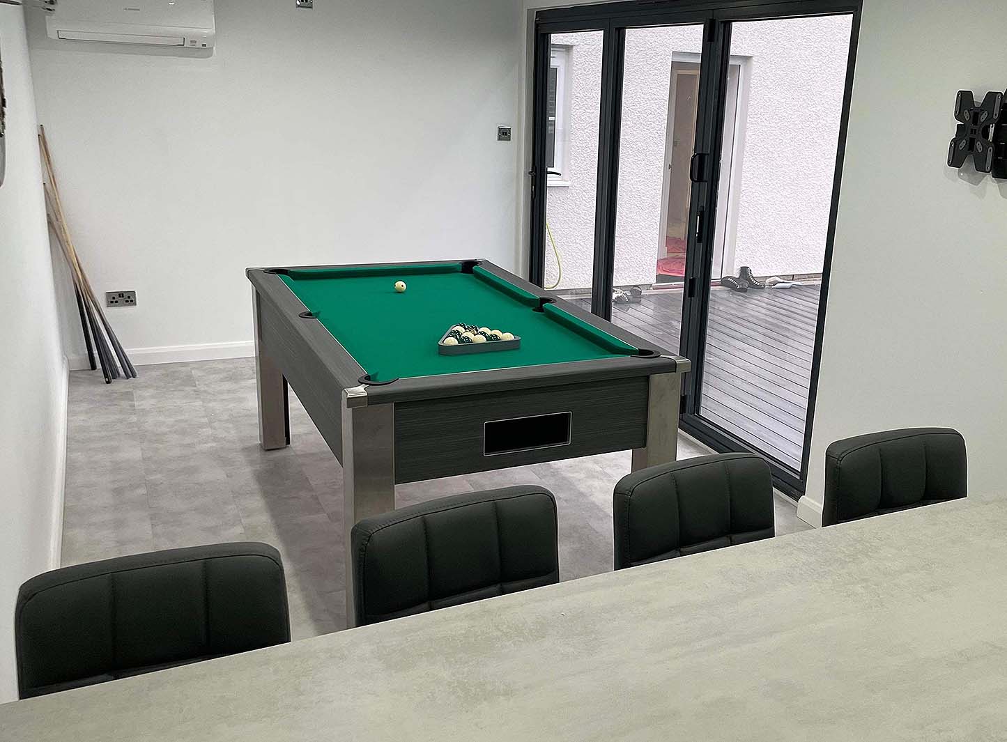 games room in a green theme with a pool table and bar with dark grey stools